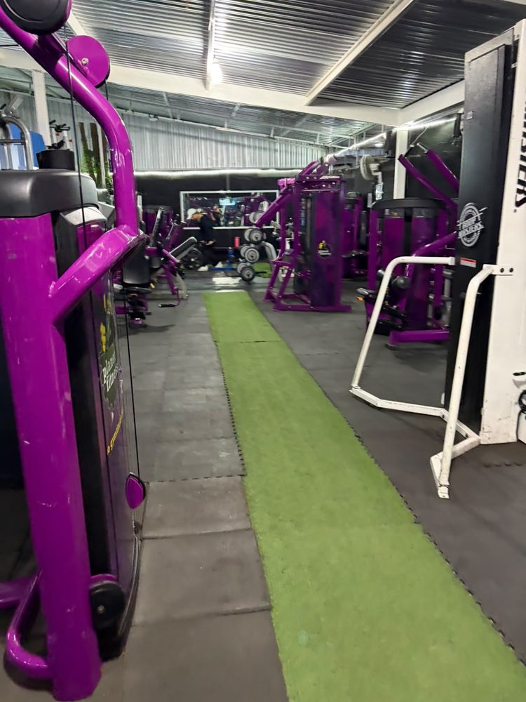 Pasillo central de GYM GOKI con tapete verde entre las máquinas moradas